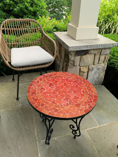 Wicker chair and a handmade Moroccan mosaic coffee table on a patio, showcasing vibrant orange Zellige tile design.