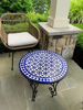 A wicker chair alongside a blue and white mosaic table, reflecting the intricate artistry of handmade Moroccan furniture.