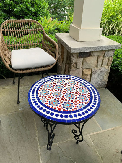 Wicker chair and a handmade Moroccan mosaic table on a patio, showcasing vibrant colors and intricate patterns.