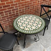 A round Moroccan mosaic coffee table with two chairs on a patio, showcasing vibrant tilework and mid-century design.