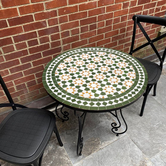 A round Moroccan mosaic coffee table with two chairs on a patio, showcasing vibrant tilework and mid-century design.