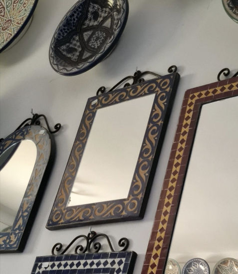 A wall adorned with decorative mirrors and plates, featuring a striking yellow and black Moroccan mosaic wall mirror.