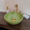 A green bowl on a wooden counter, showcasing a handcrafted Moroccan sink with intricate designs and vibrant colors.