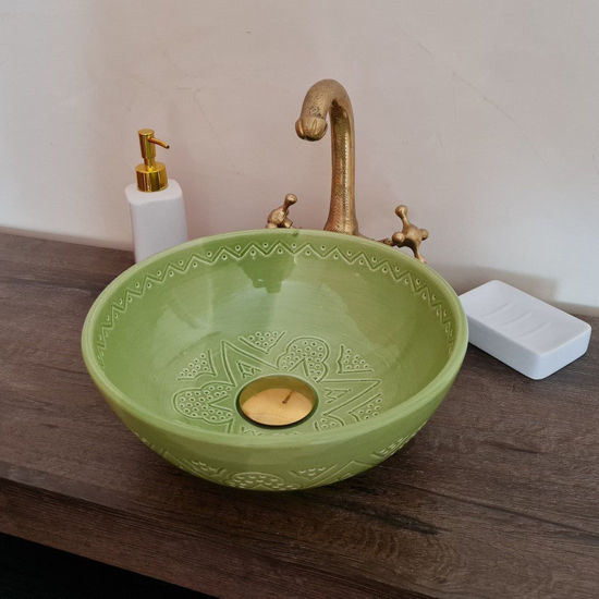 A green bowl on a wooden counter, showcasing a handcrafted Moroccan sink with intricate designs and vibrant colors.