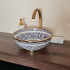 A blue and white vessel sink with gold trim rests on a wooden counter, highlighting its unique Moroccan craftsmanship.