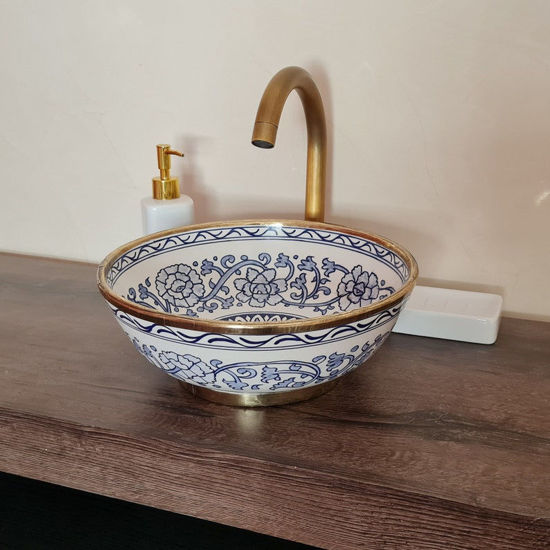 A blue and white vessel sink with gold trim rests on a wooden counter, highlighting its unique Moroccan craftsmanship.