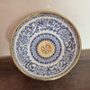 A handcrafted blue and white bowl with gold accents sits on a wooden counter, showcasing Moroccan artistry and design.