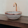 Unique white ceramic vanity sink with a solid copper trim and faucet, adorned with a handcrafted fishscale design.