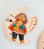 Hand-painted ceramic ornaments of an angel on a moon, crafted by Peruvian artisans for festive decor.