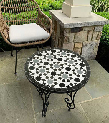 Round black and white mosaic table on a patio, featuring handcrafted Moroccan Zellige tiles that enhance outdoor decor.