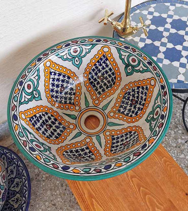 A vibrant, hand-painted Moroccan ceramic vessel sink displayed on a table, showcasing intricate patterns and rich colors.