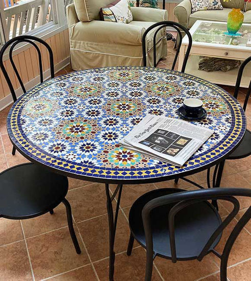 A handcrafted Moroccan mosaic table with colorful tiles, accompanied by chairs.