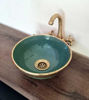 Handmade emerald green sink with aged brass faucet on a wooden counter, featuring intricate fish scale patterns and glossy finish.