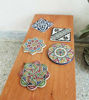 A set of four decorative Moroccan ceramic coasters on a wooden table, featuring unique hand-painted patterns and absorbent surfaces.