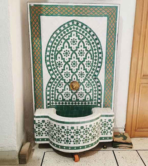 A green and white tiled Moroccan wall fountain, showcasing intricate mosaic patterns, perfect for indoor or outdoor decor.