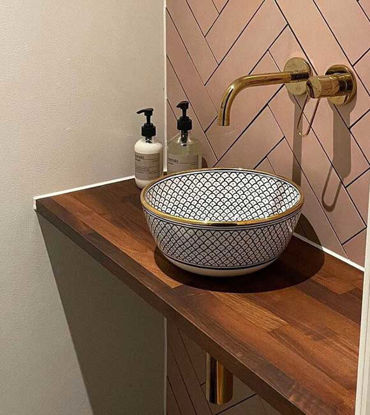 Mid-century bathroom with ceramic vessel sink and unlacquered brass wall faucet on a wooden countertop.