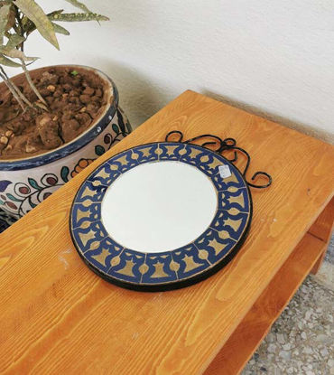 A wooden table displays a vibrant, handmade Moroccan mosaic mirror, showcasing intricate designs and colors.