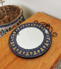 A wooden table holds a round Moroccan mosaic mirror, featuring colorful patterns and traditional craftsmanship.