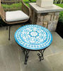 A turquoise handcrafted mosaic table with blue and white patterns, set on a patio for indoor and outdoor use.