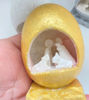 A hand grips a silver egg showcasing a detailed nativity scene, featuring Mary, Joseph, and Baby Jesus in white stone.