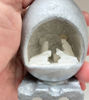 A hand holds a small silver egg containing a handcarved white stone nativity scene of the Holy Family inside.