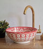 A vibrant pinkish-red Moroccan ceramic sink featuring detailed patterns and a gold faucet, perfect for a stylish bathroom or kitchen.