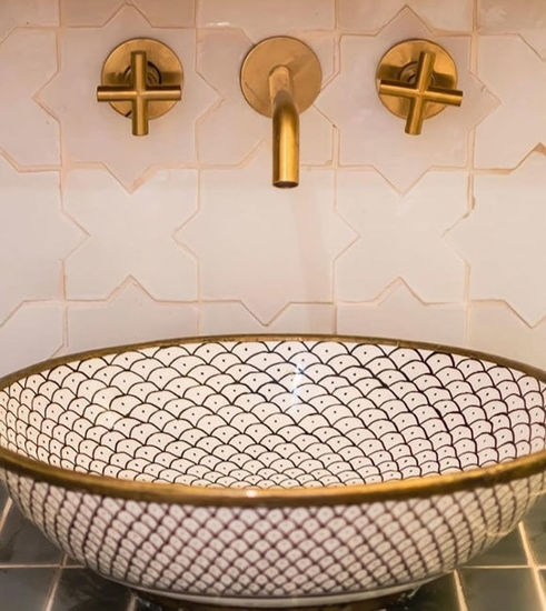 Stylish bathroom sink featuring gold fixtures against a pristine white tile wall, enhancing the room's contemporary design.