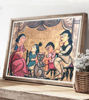 Framed Patachitra painting of a family around a table, featuring vibrant colors and a whimsical cat in a village setting.